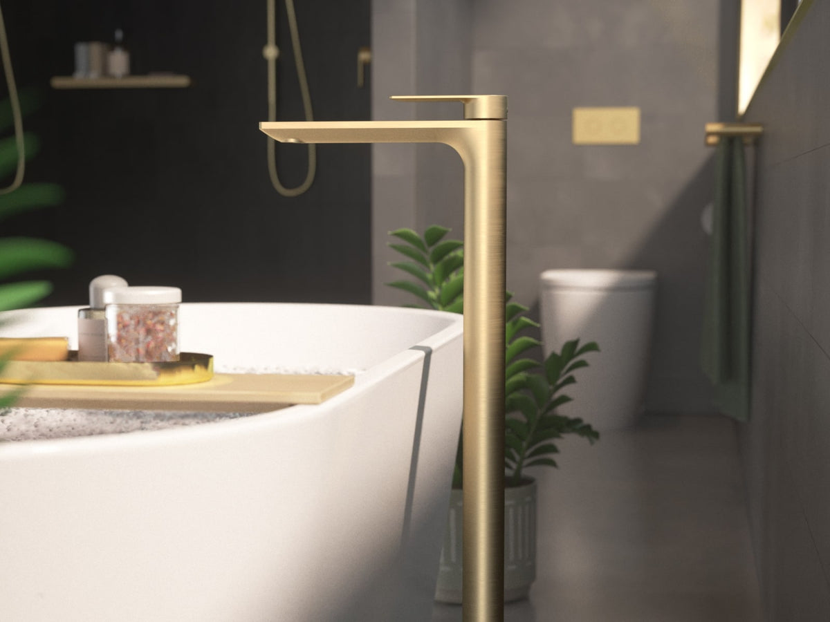Brushed brass floor mounted bath filler beside a freestanding bath