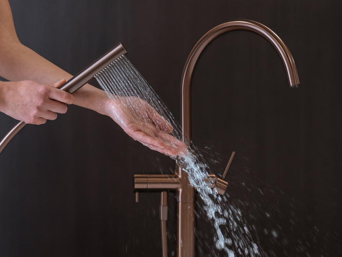Brushed copper bath filler and hand shower running over a freestanding bath
