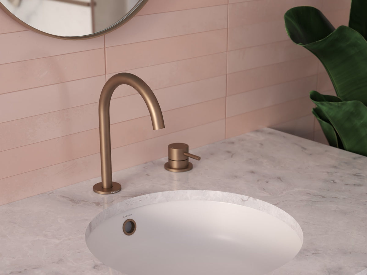 Brushed bronze gooseneck basin mixer on a marble vanity against pink tiles