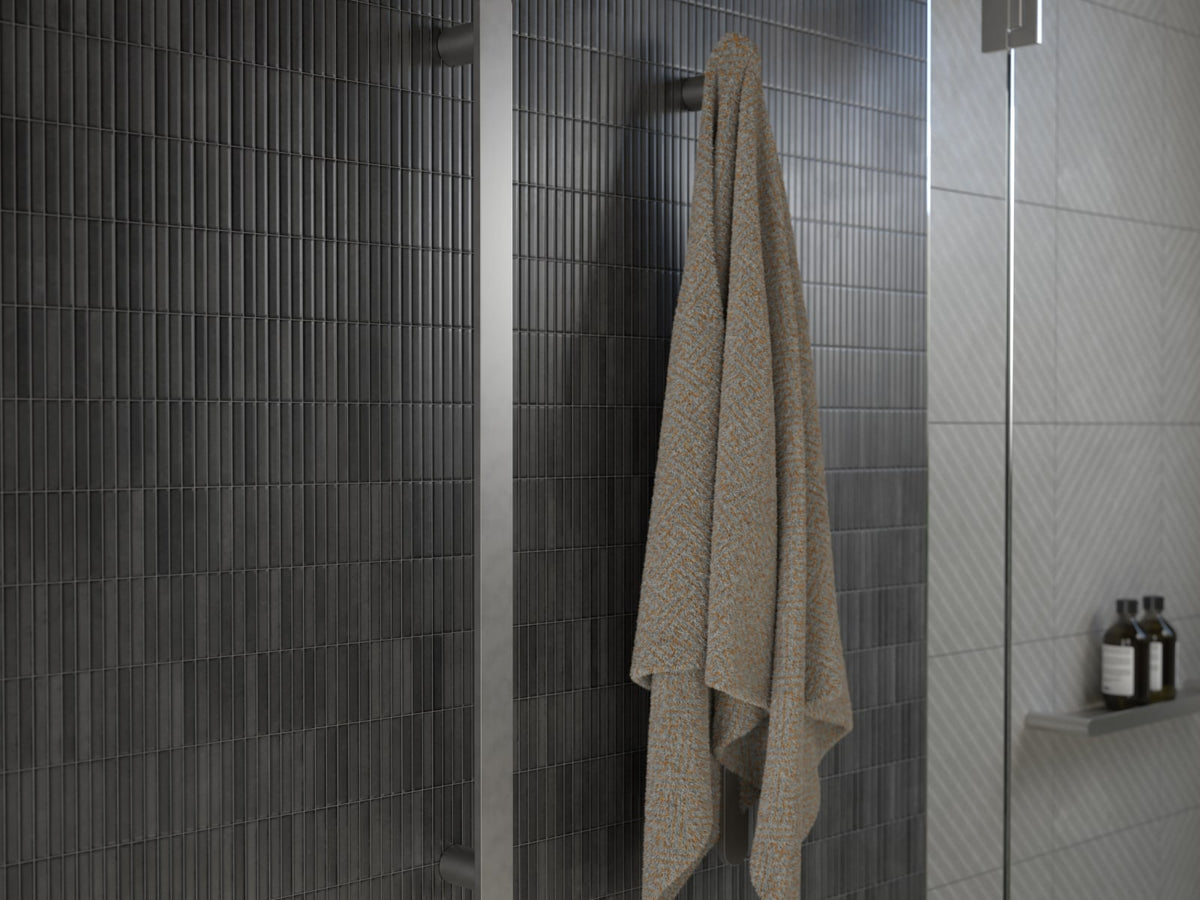 Vertical heated towel rail with a hanging towel on dark tiles